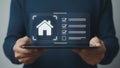 Futuristic holographic home icon with a checklist on a transparent digital interface above a tablet Royalty Free Stock Photo