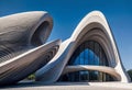 A futuristic striking architectural masterpiece, a concrete building with multiple waves, set in a modern urban landscape