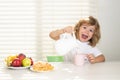 Fuuny excited little boy pouring whole cows milk for breakfast. Schoolkid eating breakfast before school. Portrait of