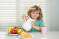 Fuuny little boy pouring whole cows milk for breakfast. Funny blonde little boy having breakfast. Milk, vegetables and