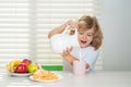 Fuuny little boy pouring whole cows milk for breakfast. Portrait of child eat fresh healthy food in kitchen at home. Kid