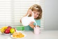 Fuuny little boy pouring whole cows milk for breakfast. Schoolkid eating breakfast before school. Portrait of child sit