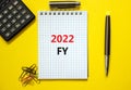 2022 FY fiscal new year symbol. White note, words 2022 FY fiscal year on beautiful yellow table, paper clips, metallic pen and