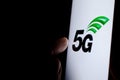 5G letters glowing on the smartphone screen and the hand reaching for it. The concept photo for 5G wireless network