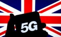 5G letters on a silhouette of a smartphone in the hand with the blurred United Kingdom flag on the background. Authentic photo, no