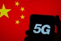 5G letters on a silhouette of a smartphone hold in hand with the flag of China on a blurred background screen. It is Authentic pho