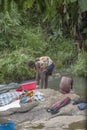 Gabela / Kwanza Sul / Angola - 02 25 2020: View of women washing clothes in river waters with her son in backs, rocks and herbs on