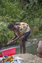 Gabela / Kwanza Sul / Angola - 02 25 2020: View of women washing clothes in river waters with her son in backs, rocks and herbs on