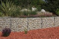 Gabion retaining wall with pebble-topped wire mesh reinforcement in a flower-filled green space mulched with bricks Royalty Free Stock Photo