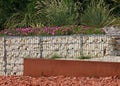 Gabion retaining wall with pebble-topped wire mesh reinforcement in a flower-filled green space mulched with bricks Royalty Free Stock Photo