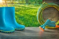 Gadening tools in spring sunny garden at sunrise blue rain rubber boots and hose with spray gun