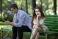 Gadget addiction. Bored young girl and her boyfriend stuck in cellphone on dull date at park