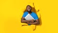 Gadget lover. Happy black man hugging laptop computer and smiling, posing in torn hole of yellow paper background Royalty Free Stock Photo