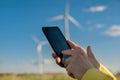 Gadget with a program for monitoring technical parameters in focus in human hands on a blurred background of wind turbines