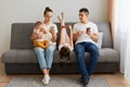 Gadgets addiction. Young family of holding and using different electronic devices while sitting on sofa. Parents and their