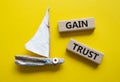 Gain trust symbol. Wooden blocks with words Gain trust. Beautiful yellow background with boat. Business and Gain trust concept.