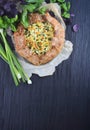 Galette with egg, green onion, cheese and crispy vegetarian dough on a black wooden table and wooden background.