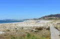 Beach with vegetation in sand dunes, boardwalk, river and lighthouse. Blue sea with waves and foam, sunny day. Galicia, Spain. Royalty Free Stock Photo