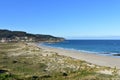 Beach and sand dunes with morning light. Rocks and blue sea with small waves and foam. Sunny day, clear sky. Galicia, Spain. Royalty Free Stock Photo