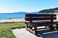 Bench on a beach promenade with grass and vegetation in sand. Blue sea, clear sky, sunny day. Galicia, Spain. Royalty Free Stock Photo