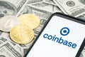 Coinbase logo on Smartphone screen and dollar banknotes and bitcoin and ethereum coins