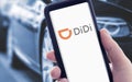 Hand holding a smart phone with DIDI logo on screen and blurry cars on background