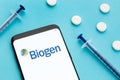 Smart phone showing Biogen logo on screen and pills and syringe on blue background