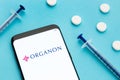 Smart phone showing Organon logo on screen and pills and syringe on blue background