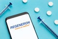 Smart phone showing Regeneron logo on screen and pills and syringe on blue background