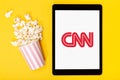 Popcorn bucket and tablet with CNN logo on yellow background. Top view