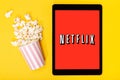 Popcorn bucket and tablet with Netflix logo on yellow background. Top view