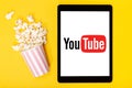 Popcorn bucket and tablet with Youtube logo on yellow background. Top view