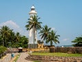 Galle, Sri Lanka - March 12, 2022: View of the white stone lighthouse and tall coconut palms at Galle Fort. Tourists walk and take Royalty Free Stock Photo