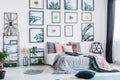 Gallery with simple posters hanging on the wall in bright bedroom interior with many pillows on bed, fresh plants and plastic chai Royalty Free Stock Photo