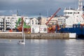 Galway/Ireland- 10/11/2020: Small yacht sailing in river Corrib, Galway port with commercial ships in the background