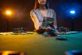 Gambler woman siting at the table in casino and throws cards above the table. Lucky player on smoky background with lamps. Concept