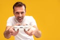 Gambling addiction. Excited mature man holding joystick and playing video games, looking at the camera and smiling.  Yellow studio Royalty Free Stock Photo