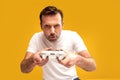 Gambling addiction. Excited mature man holding joystick and playing video games, looking at the camera.  Yellow studio background Royalty Free Stock Photo