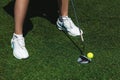 The game of golf. A girl in white sneakers holds a club and a ball against the green field. Close-up. Female golf player at golf c Royalty Free Stock Photo