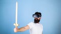 Gamer concept. Guy with head mounted display holds sword, play fighting game in VR. Hipster on serious face enjoy play Royalty Free Stock Photo