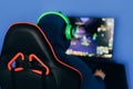 The gamer sits on a gaming chair and plays computer games. The player has green headphones on his head Royalty Free Stock Photo