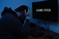 Gamer wearing headphones, sad because he has lost the video game. Game over on computer screen