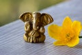 Ganesha figure with bright yellow flower closeup. Beautiful Ganesh statue with open palm and blooming flower on wooden board.