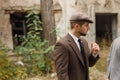 Gangster looks at someone, standing by the abandoned building. Retro. Outdoors.