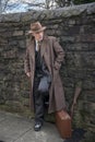 Gangster with a rifle gun and suitcase, posing outdoors.