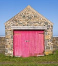 Garage made of Welsh stone with worn pink wooden doors. UK