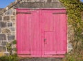 Garage made of Welsh stone with worn pink wooden doors. UK