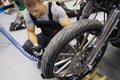In garage, a repairman in overalls sits near wheel motorcycle
