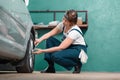 Garage. Young woman mechanic in blue coveralls squatting and repair tire with ratchet wrench. The concept of Royalty Free Stock Photo