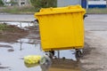 Garbage in bags lies next to a garbage container in a dirty puddle. Trash can full of waste. Royalty Free Stock Photo